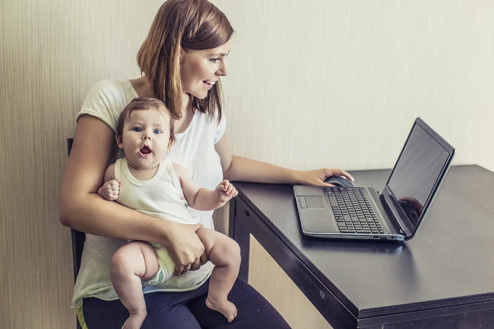 Woman working on laptop with infant in her lap.
