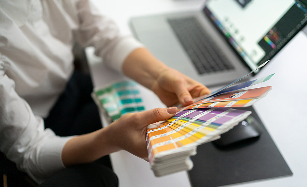 Woman holding color swatches next to a laptop.