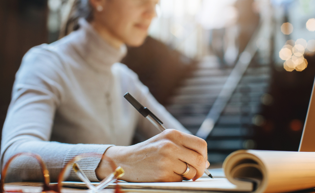 Woman writing with pen on a pad of paper outside.