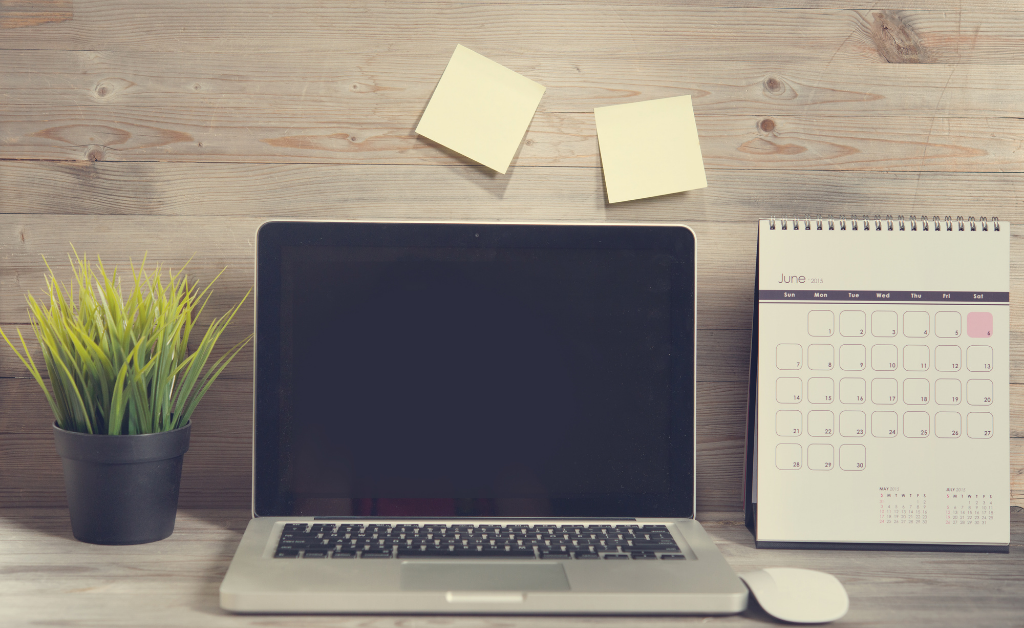 Open laptop on desk with sticky notes and a calendar.