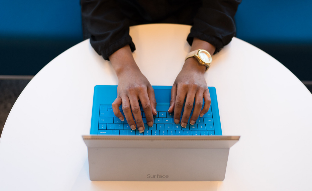 Black man on blue laptop on a round, white table.