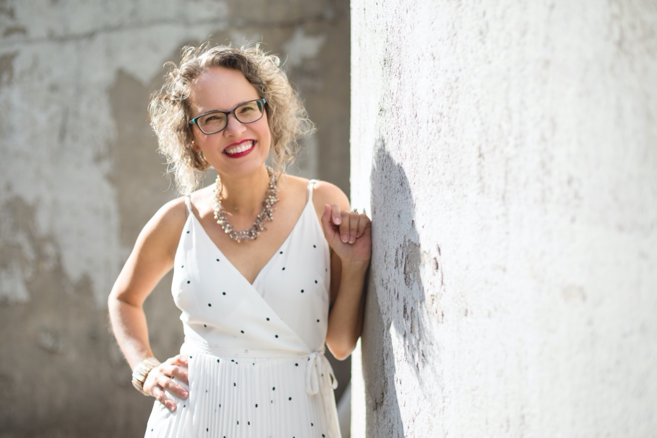 Lidia leaning against a wall in a white dress.