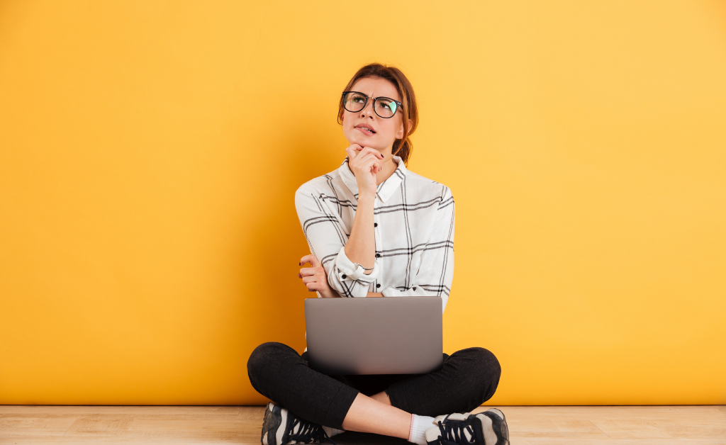 Woman sitting cross-legged on the floor with a laptop with a yellow wall.