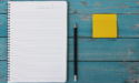 Notebook, pencil, and yellow sticky note on a teal table.
